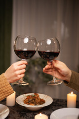 Close-up of hands of man and woman holding glasses of red wine, having dinner in restaurant, celebrating Valentine's Day