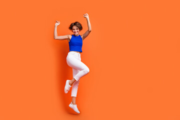 Fototapeta na wymiar Full body portrait of gorgeous cheerful lady jumping raise hands empty space ad isolated on orange color background