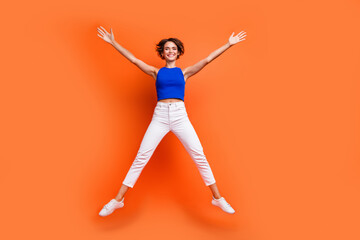 Full size portrait of overjoyed energetic girl jumping raise hands make star figure isolated on orange color background