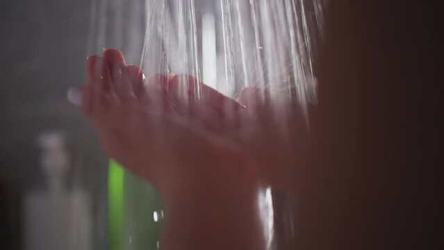 Woman finds solace in gentle cascade of hot water. Young woman cupping hands under flowing stream in shower. Lady stands under warm water in shower