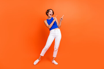 Full size portrait of astonished pretty girl look direct fingers empty space information isolated on orange color background
