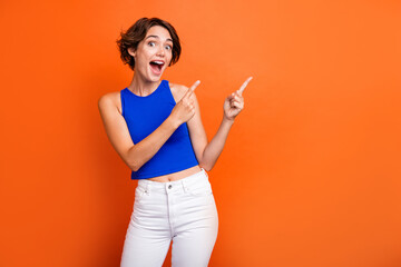 Photo of adorable impressed lady wear blue singlet open mouth pointing two fingers empty space isolated orange color background