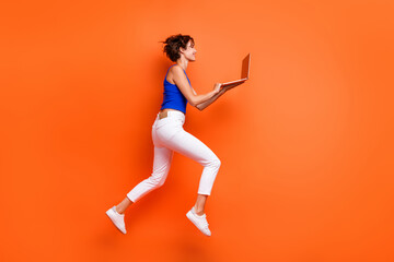Full body profile portrait of excited charming lady jump run use netbook isolated on orange color background - obrazy, fototapety, plakaty