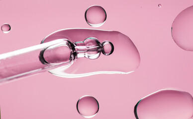 Cosmetic dropper with serum, beauty cosmetics dripping, on pink background. Macro shot. Serum, peptides, beauty and health care products. Glass pipette with liquid, close up. Top view. Skin care