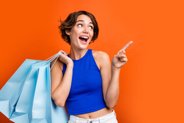 Portrait of attractive impressed girl hold store bags look direct finger empty space advert isolated on orange color background - obrazy, fototapety, plakaty