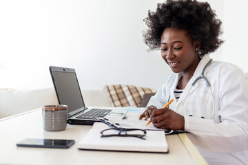 Serious concentrated African American doctor working in her office at clinic. Hardworking African American doctor writing diagnosis in doctor's office.