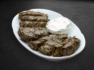 Dolma with lamb and white sauce. Grape leaves with minced meat. Oriental cuisine. Isolated on a dark background