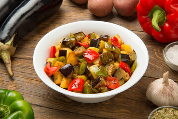 Fried eggplants, potatoes and bell peppers on a rustic wooden table with ingredients. - 671580741