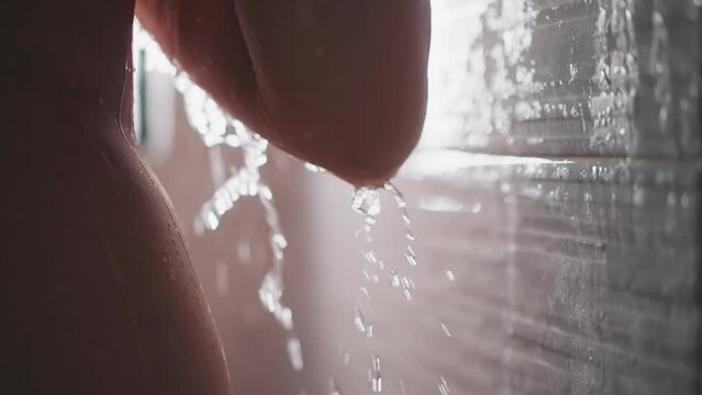 Bare woman with falling down water sprays in bathroom closeup. Skinny lady stands under pure shower jets in washroom. Relaxation and body washing