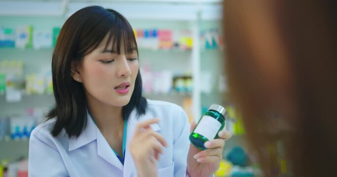 Young Asian pharmacist talking with customer at pharmacy counter. She tells customers about drug information at the pharmacy.