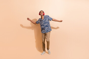 Full length photo of satisfied man dressed stylish shirt dancing in headphones look empty space isolated on beige color background