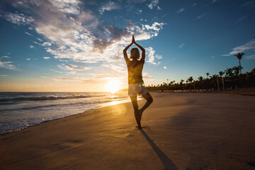 Middle-aged woman does yoga on the beach at dawn