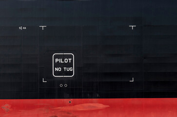 Close up of section of the black and red hull of a ship with letters PILOT No Tug 