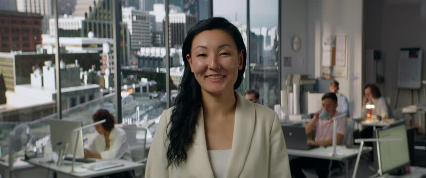 Portrait of Asian female office smiling is posing to the camera, busy office in the background