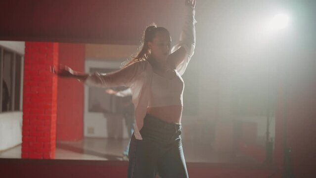 Young attractive woman is dancing hip hop contemporary in dace hall close-up on white light. Shooting of modern slow dance choreography. Motion of female dancer expressing feelings in dance movings. 