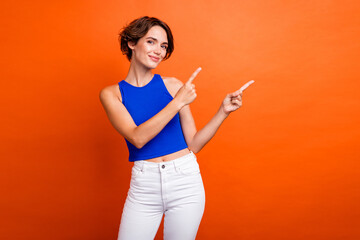 Photo of sweet adorable lady wear blue singlet pointing two fingers empty space isolated orange color background