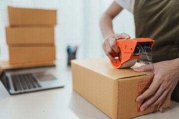 Entrepreneur female using adhesive tape packing box at home office. Technology online marketing and...
