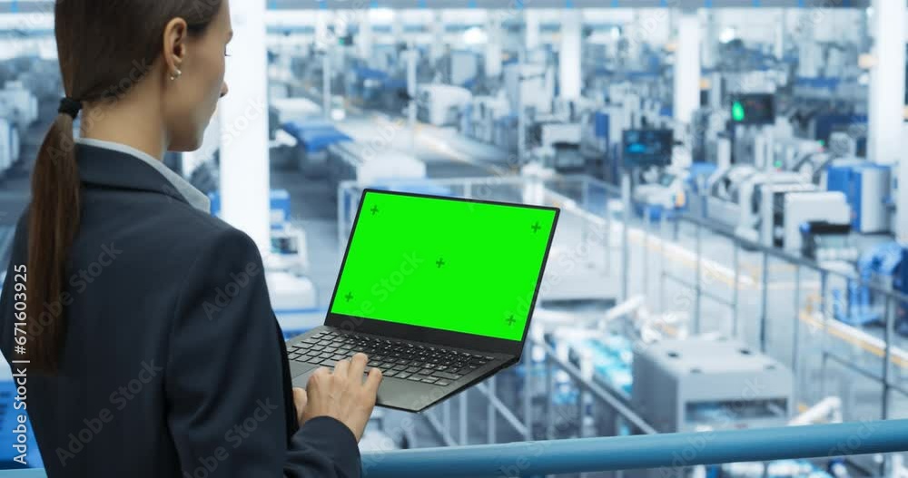 Poster Young Female Engineer Using Laptop Computer with Green Screen Mock Up Display at an Electronics Factory. Over the Shoulder Footage. Automated Manufacturing Machines and AI Robots Are Monitored Online