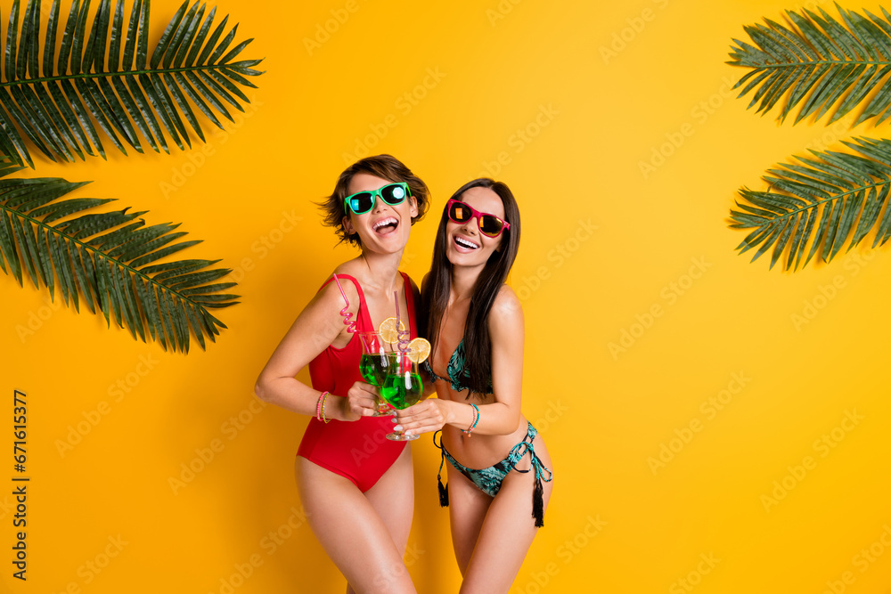 Poster Photo of funky good mood girls dressed swimsuits enjoying alcohol cocktails empty space isolated yellow color background