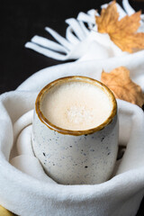 Pumpkin latte in scarf with fall leaves and cinnamon. Warm beverage during cold weather