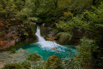 Naklejka na ściany i meble The waterfalls and crystal clear, blue, turquoise and green waters of the Nacedero del Urederra, with its beech forest with its autumn colors in the Sierra de Urbasa-Andía. Navarre. Spain