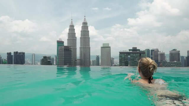 women is swimming in a infinity rooftop pool and is looking over the skyline from kuala lumpur, malaysia