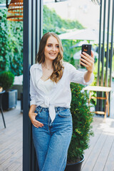 cute young woman in jeans and a white casual shirt is talking on the phone. Video communication via telephone. Remote freelance work.