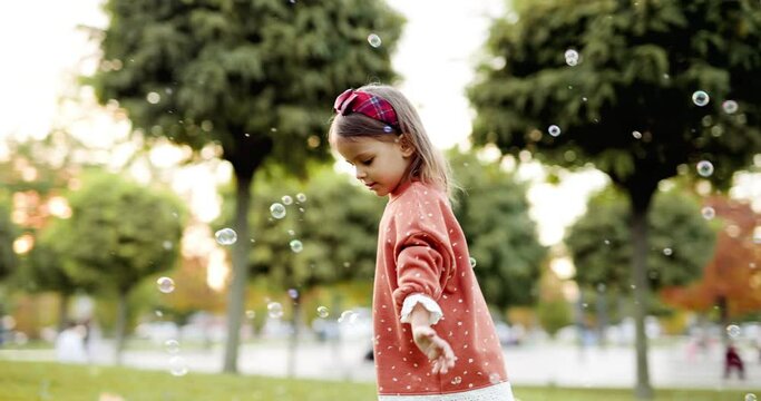 Cute little girl in an autumn park playing with soap bubbles on the grass. Toddler having fun outdoor. Autumn lifestyle photo for advertising tape.