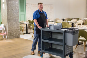 A restaurant worker pushes a cart to collect dirty dishes.
