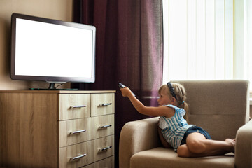 Little girl child 5-6 year old lying down on chair with remote control watching tv, empty isolated...