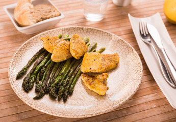 Fried chicken breast pieces with asparagus on white plate