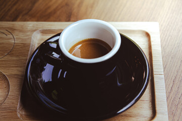 High angle of cup of hot aromatic espresso placed on black saucer over wooden table.