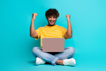Full body portrait of delighted person sit floor use wireless netbook raise fists isolated on turquoise color background