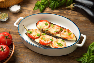 Caprese of baked eggplant tomato and mozzarella in an oval baking dish on a rustic wooden table with ingredients.  - 671624595