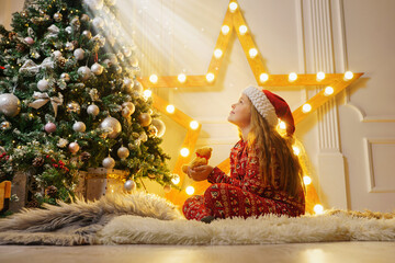 Little girl with plush toy as a friend on Christmas evening looking at the holy light. Believe in...