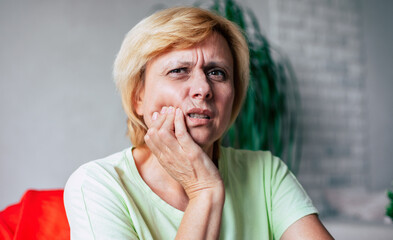 Dental care. Dentistry. Tooth health. Close up portrait of a stressed middle aged woman pressing her cheek while struggling and suffering with a strong and severe toothache