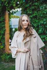 Portrait of a beautiful young woman in a light beige dress. Romantic woman in a dress with a smile on her face on the background of a green garden. Women's cocktail dress for a holiday