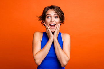 Photo of excited funky lady wear blue singlet arms cheeks open mouth isolated orange color...