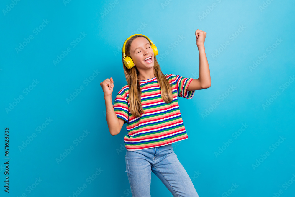 Sticker Photo of funny adorable schoolgirl dressed striped t-shirt listen playlist in headphones dancing isolated on blue color background