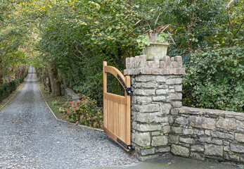 Gate post with wooden gate open to a long driveway