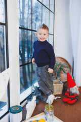 A 2-year-old boy sits by the window in the New Year. New Year's atmosphere at home. The child is waiting for the new year.