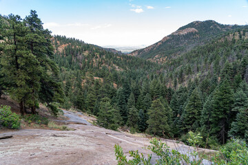 View from North Cheyenne Cañon Park in Colorado Springs, CO in the late afternoon on a sunny summer day, with trees, red rocks, and mountains in the landscape