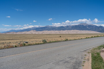 A road leading to Great Sand Dunes National Park in Colorado on a sunny summer day, with mountains in the background