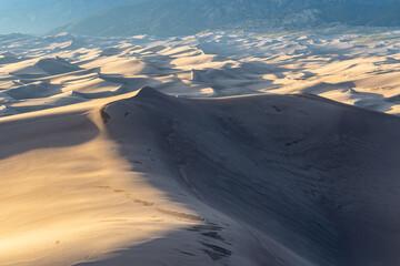 View from the top at golden hour at Great Sand Dunes National Park in Colorado on a sunny summer evening, with mountains in the background