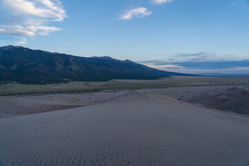 View from the top at golden hour and sunset at Great Sand Dunes National Park in Colorado on a sunny summer evening, with mountains in the background
