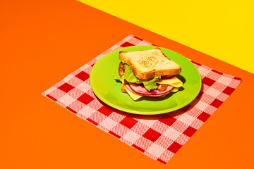 Plate with club sandwich with grilled bread, ham, lettuce, cheese, tomato and avocado on checkered...