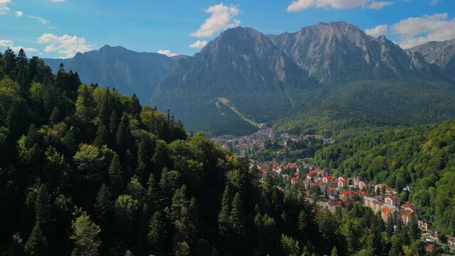 Astonishing aerial view with the rocky mountains filmed in cinematic style. Romanian landscape above Busteni city in a sunny day with blue sky
