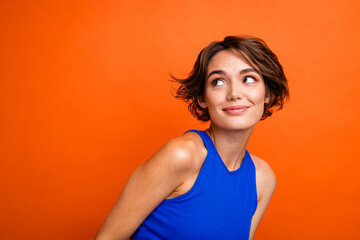 Photo of cute dreamy lady wear blue singlet smiling looking empty space isolated orange color background