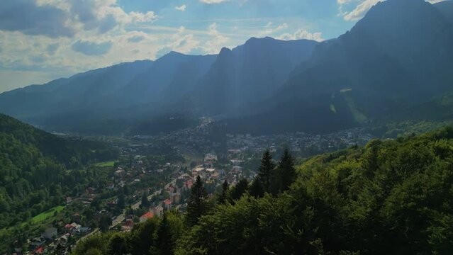 Astonishing aerial view with the rocky mountains filmed in cinematic style. Romanian landscape above Busteni city in a sunny day with blue sky