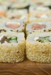 Close-up of a lot of sushi rolls with different fillings lie on a wooden surface. Macro shot of cooked classic Japanese food with a copy space.